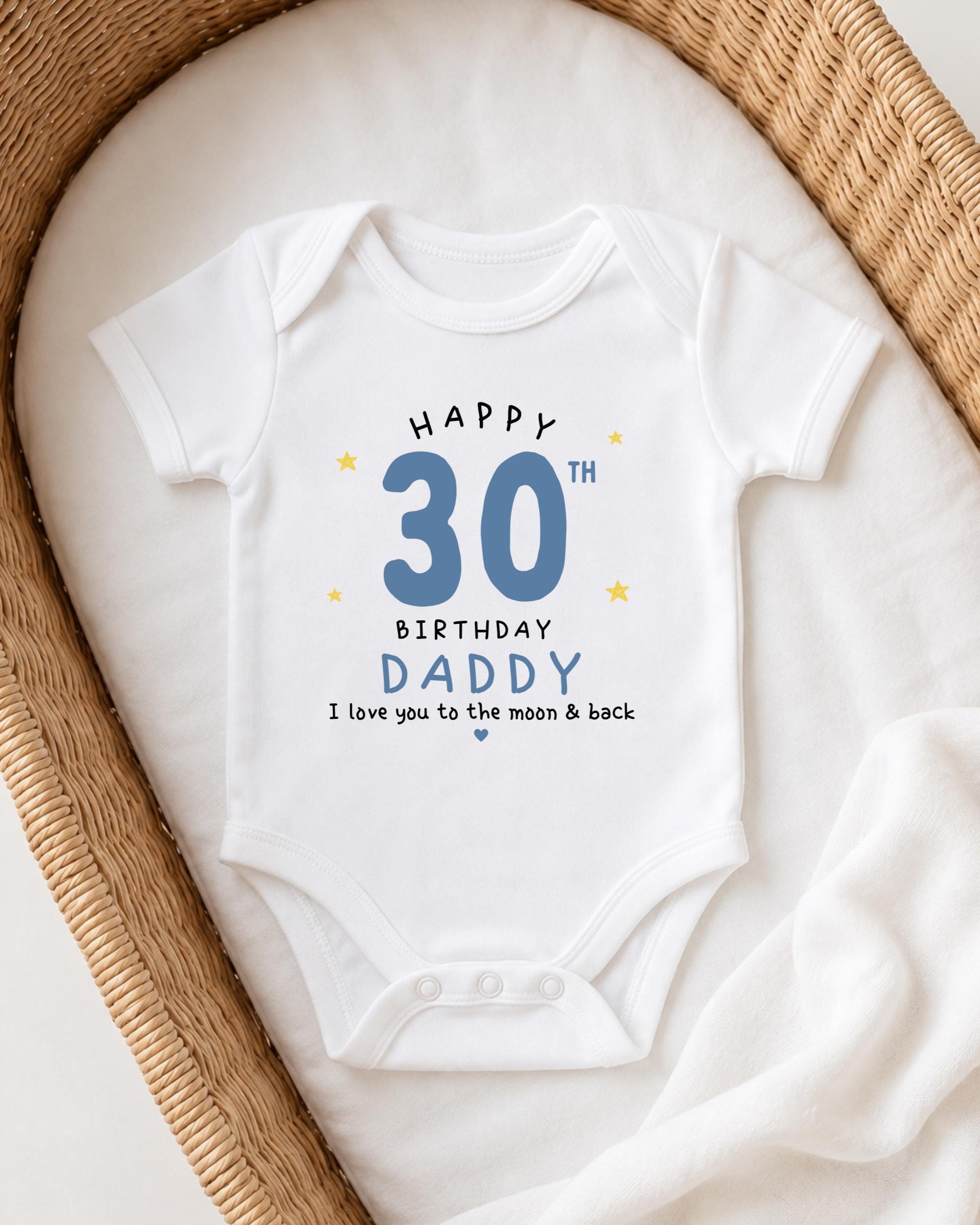 A white onesie with a birthday message printed on it, placed in a woven basket.