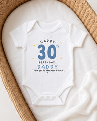 A white onesie with a birthday message printed on it, placed in a woven basket.