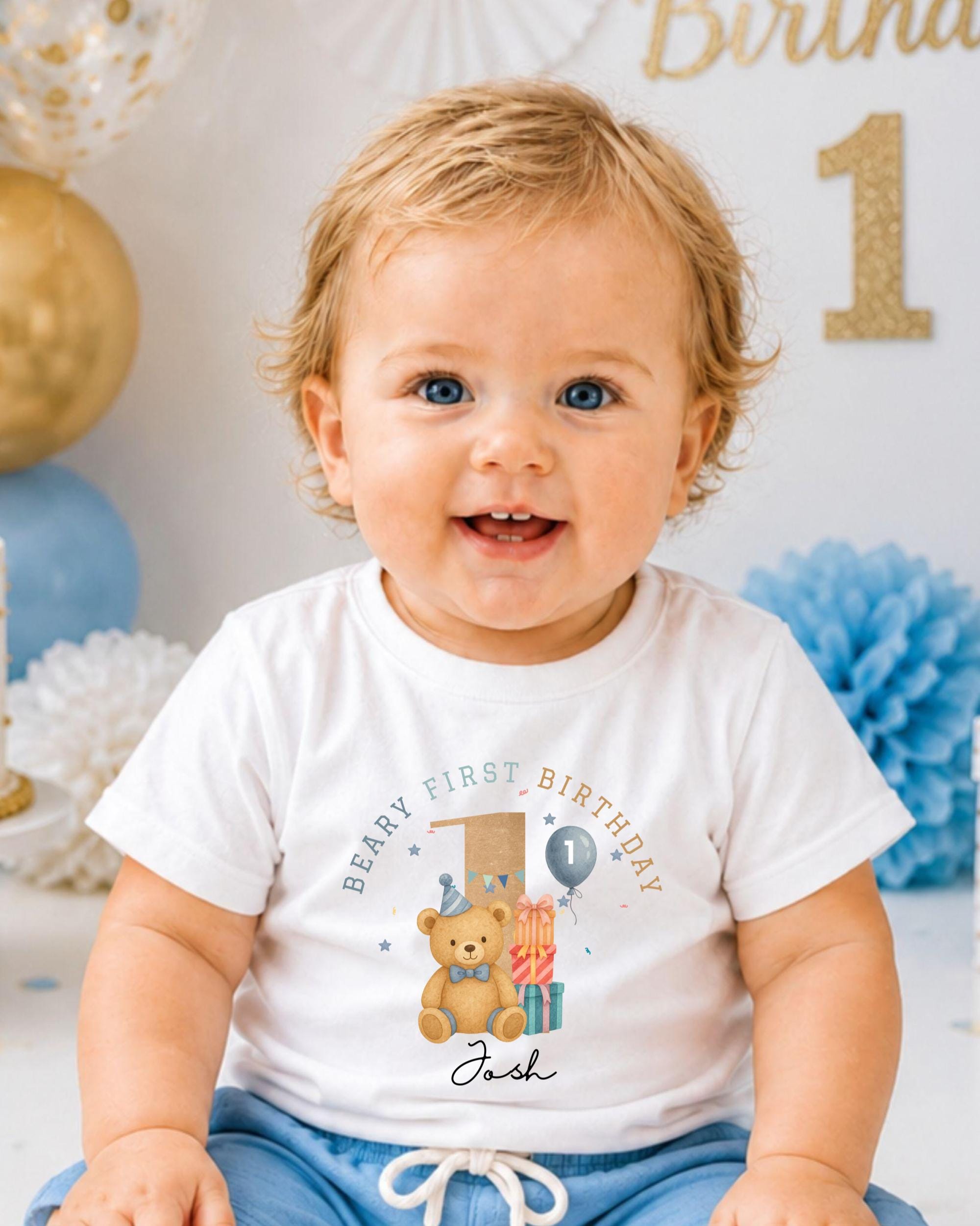A smiling baby boy wearing a white t-shirt with a teddy bear and the text "Beany first birthday Jack" printed on it.