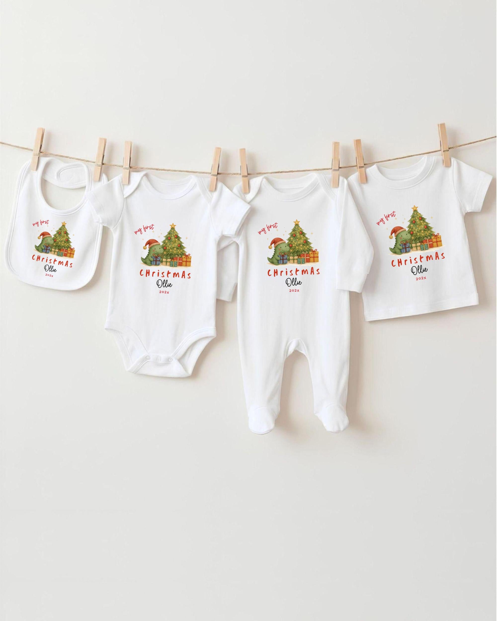 A row of four white Christmas-themed baby clothes, including bibs and onesies, hanging on a clothesline.