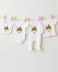 A row of four white Christmas-themed baby clothes, including bibs and onesies, hanging on a clothesline.