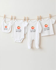 a collection of four white baby clothes hanging on a clothesline, each with a tomato printed on it.