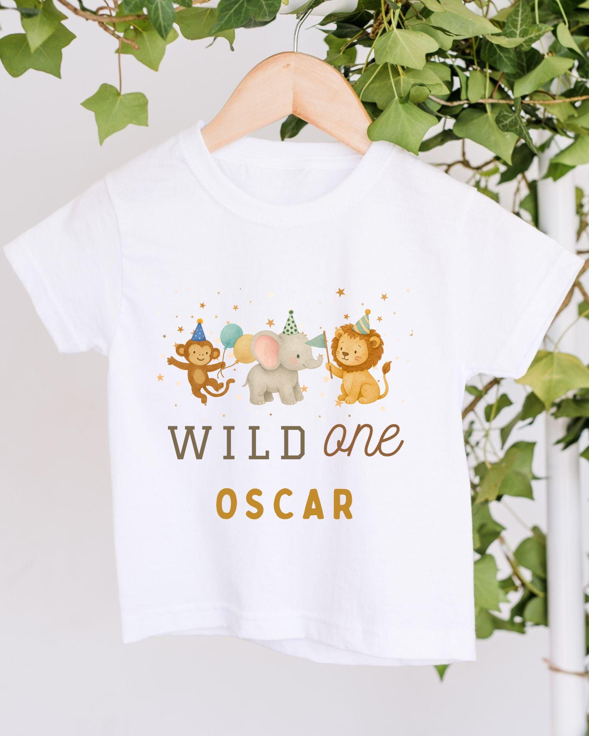 A white t-shirt with a graphic design featuring three cartoon animals - a lion, an elephant, and a monkey - along with the text "WILD one OSCAR" printed on it.