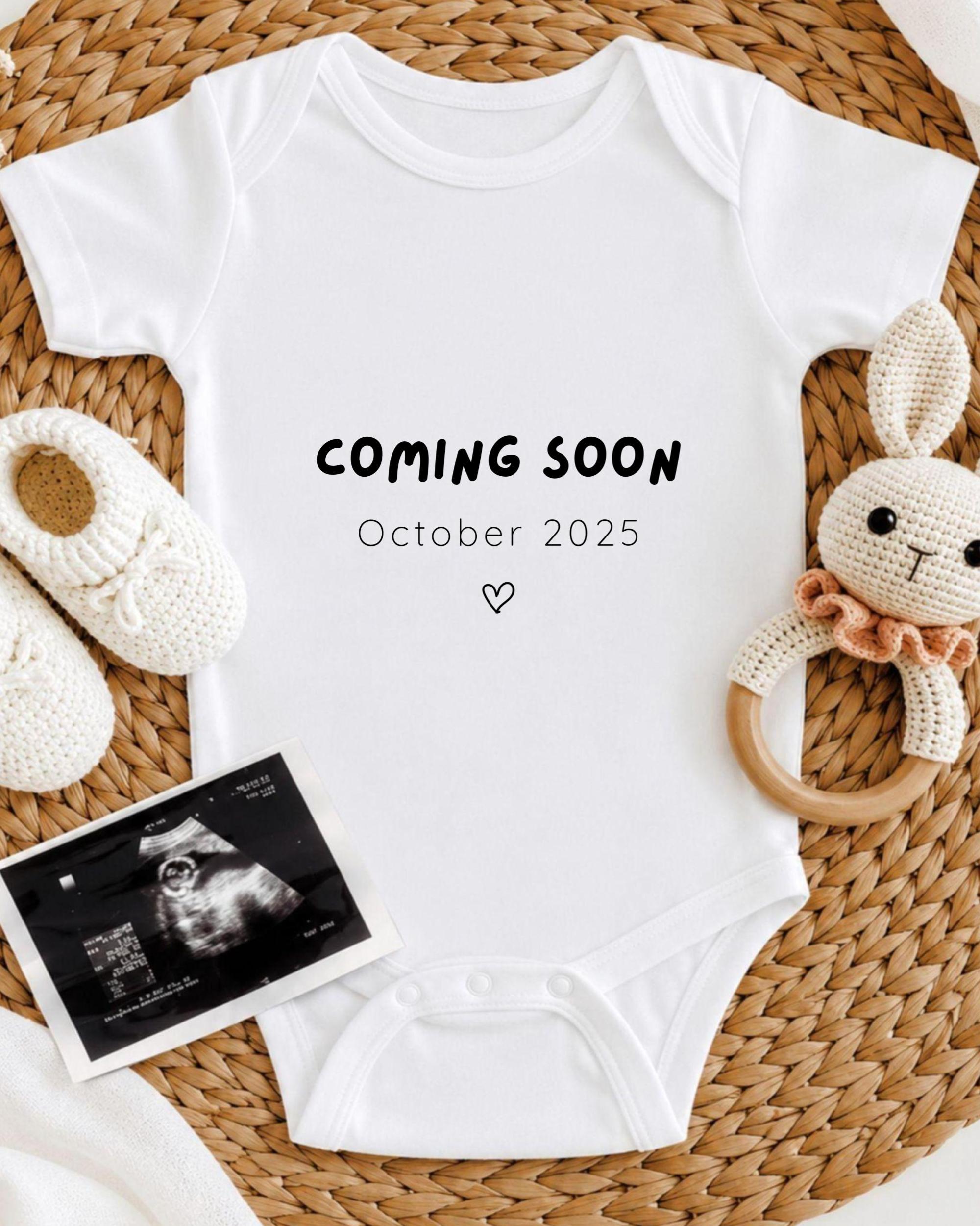 a white onesie with the text "COMING SOON October 2025" printed on it, along with a crocheted bunny toy and a black and white photograph of an infant's head.