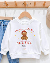 A white sweatshirt with a teddy bear graphic and text printed on it, hanging on a wooden hanger.