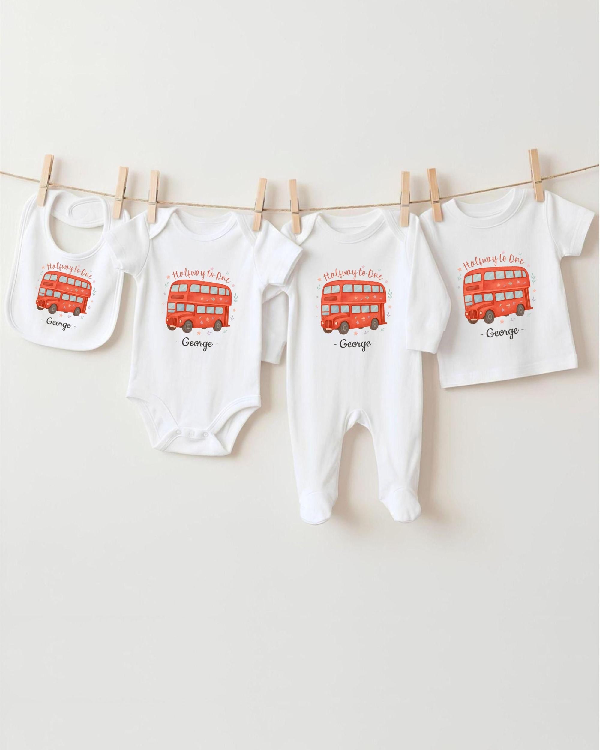 A row of four white baby clothes with red double-decker bus designs, each with a personalized name printed on it.