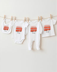 A row of four white baby clothes with red double-decker bus designs, each with a personalized name printed on it.