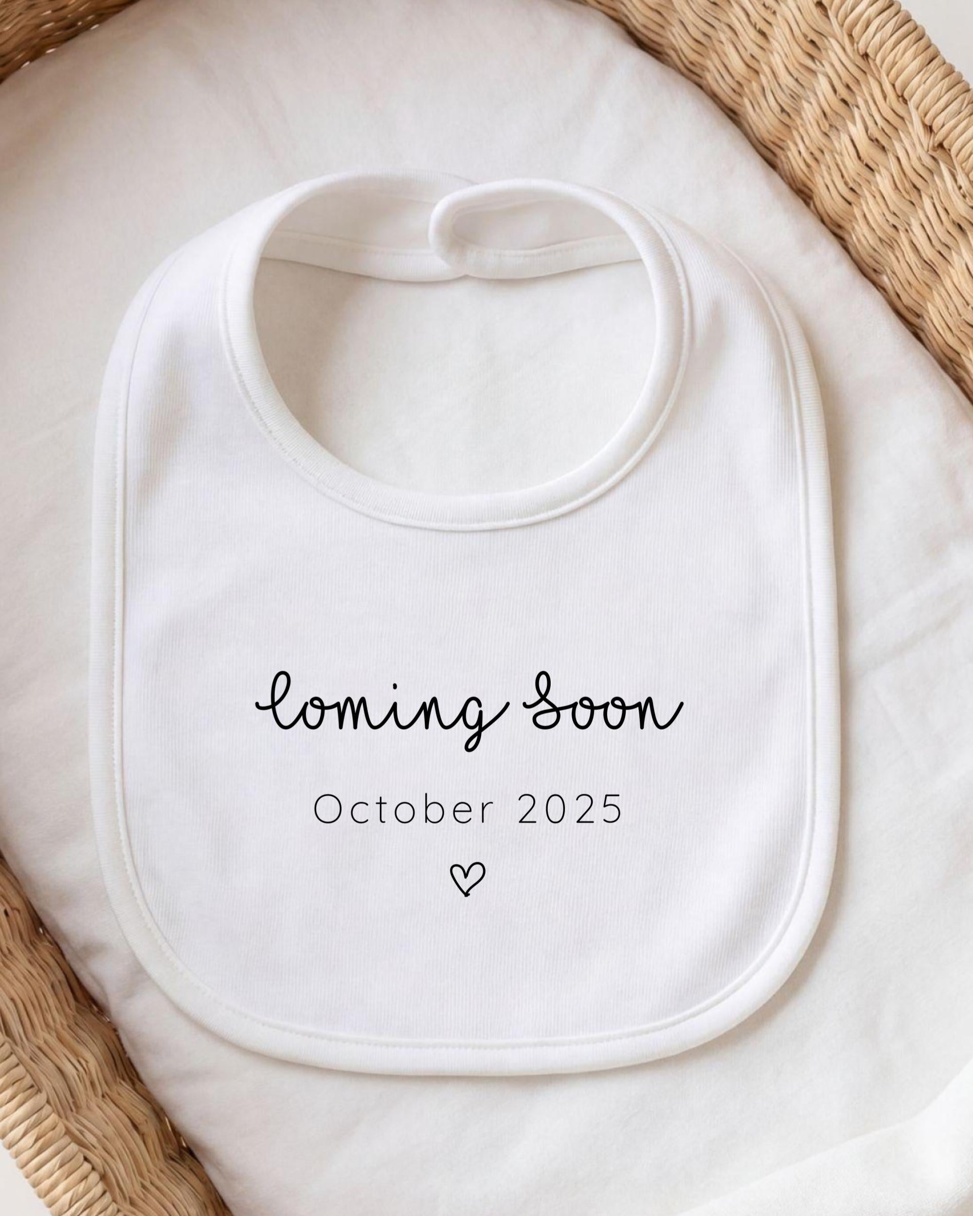 A white bib with the text "coming soon October 2025" printed on it, placed on a white cloth.