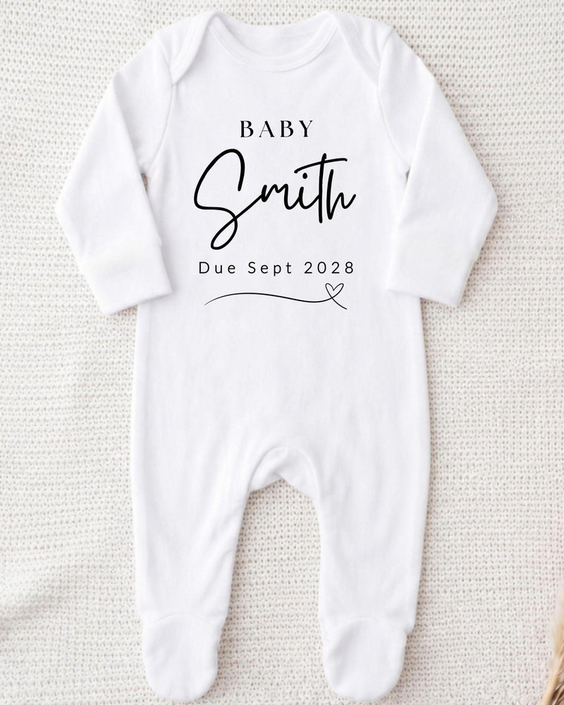 Personalisable white Baby Grow for a pregnancy announcement, printed in black with 'Baby Smith Due Sept 2028' and a fine-line heart.