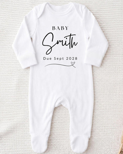 Personalisable white Baby Grow for a pregnancy announcement, printed in black with 'Baby Smith Due Sept 2028' and a fine-line heart.