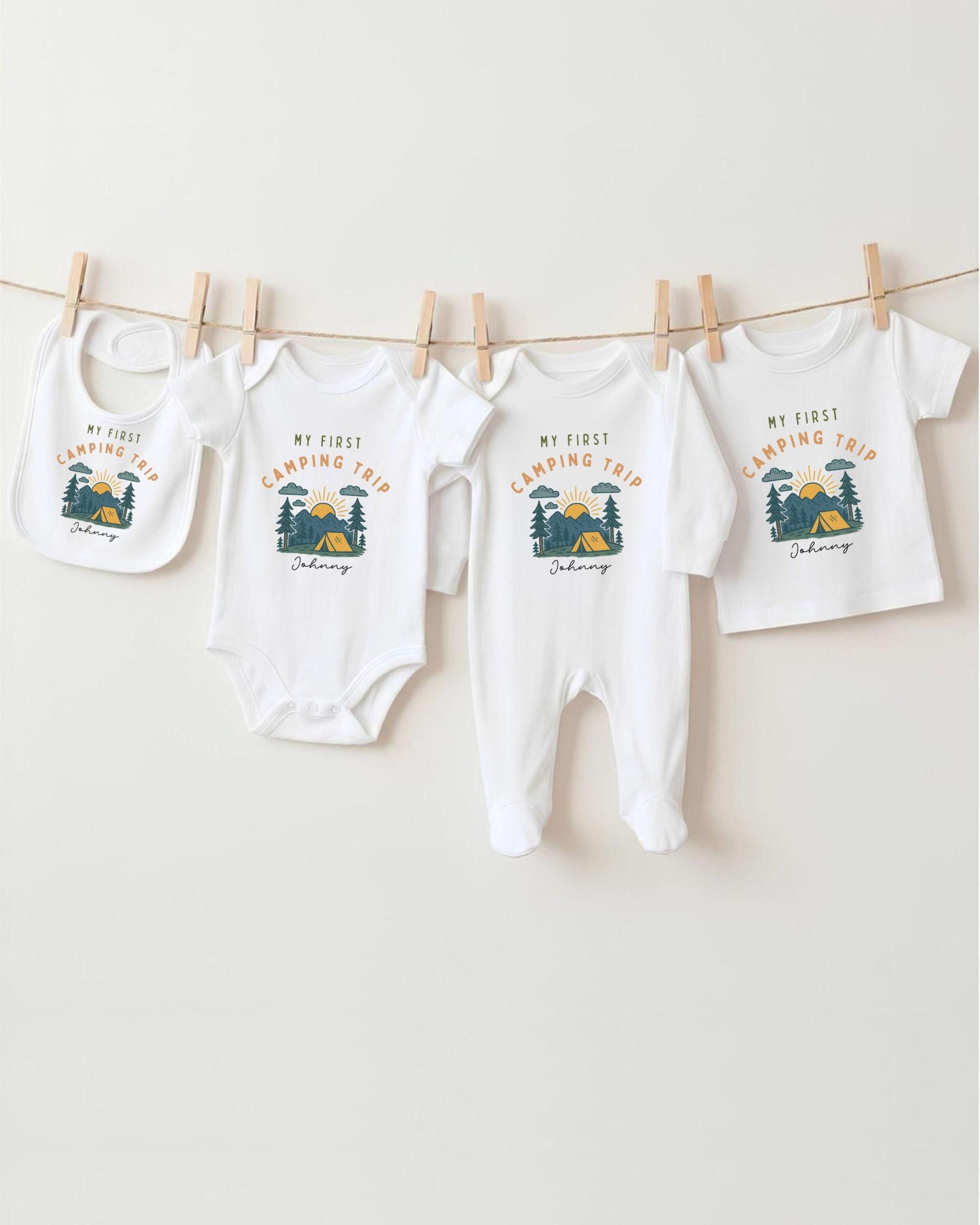 A collection of four white baby clothes, including onesies and bibs, hanging on a clothesline.