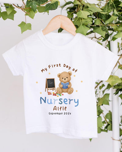 A white t-shirt with a teddy bear and a chalkboard, along with the text "My First Day of Nursery Aifie" and "September 2023".