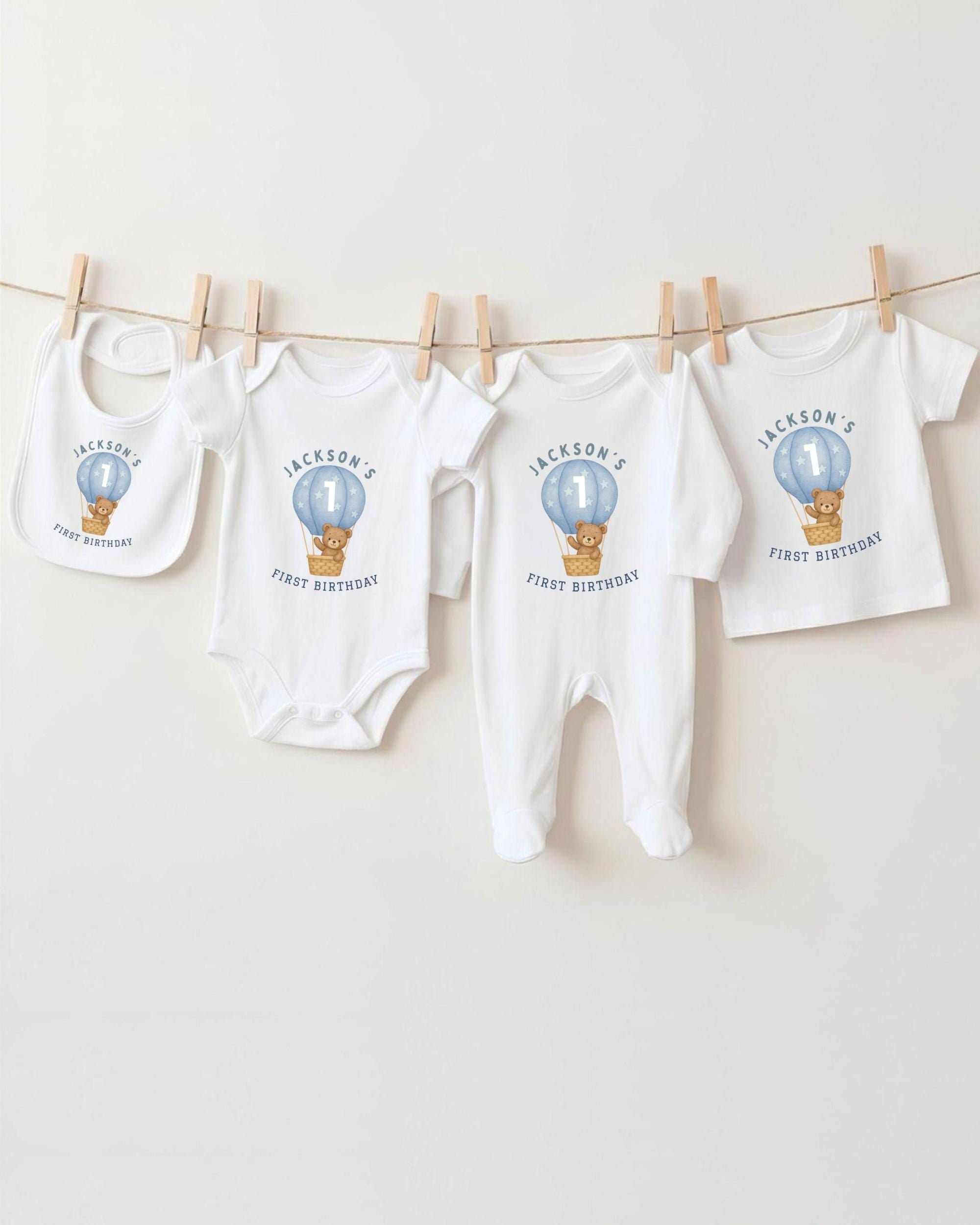 A collection of white baby clothes, including onesies and bibs, with a unique design featuring a teddy bear and a hot air balloon.
