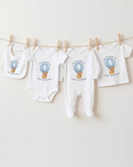 A collection of white baby clothes, including onesies and bibs, with a unique design featuring a teddy bear and a hot air balloon.