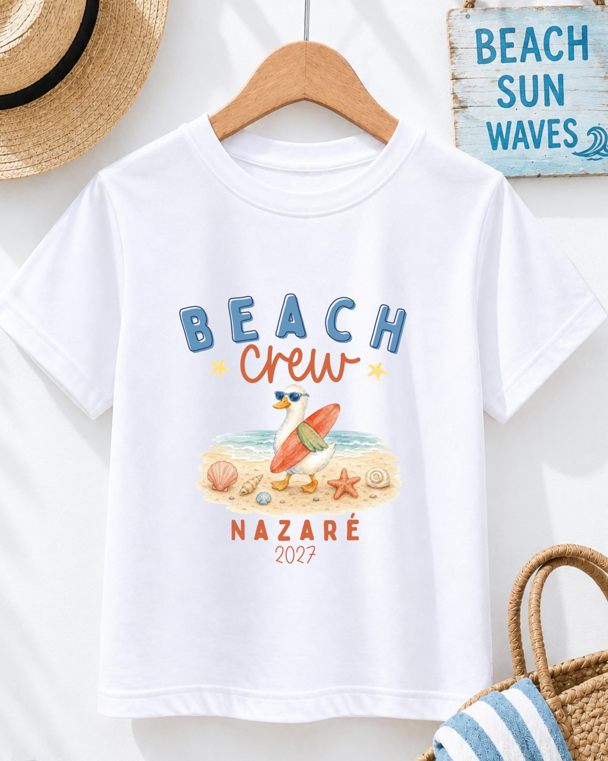 A white t-shirt with a beach-themed graphic design, including a surfer, beach elements, and text that says "BEACH CREW".