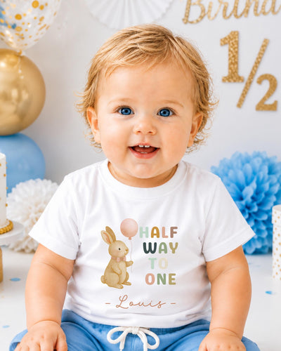 A smiling baby boy wearing a white t-shirt with a cartoon rabbit and the text "Half Way to One" printed on it.