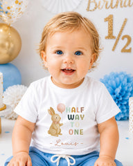 A smiling baby boy wearing a white t-shirt with a cartoon rabbit and the text "Half Way to One" printed on it.