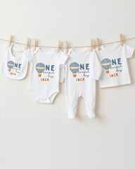 A collection of baby clothes, including onesies and pants, hanging on a clothesline.
