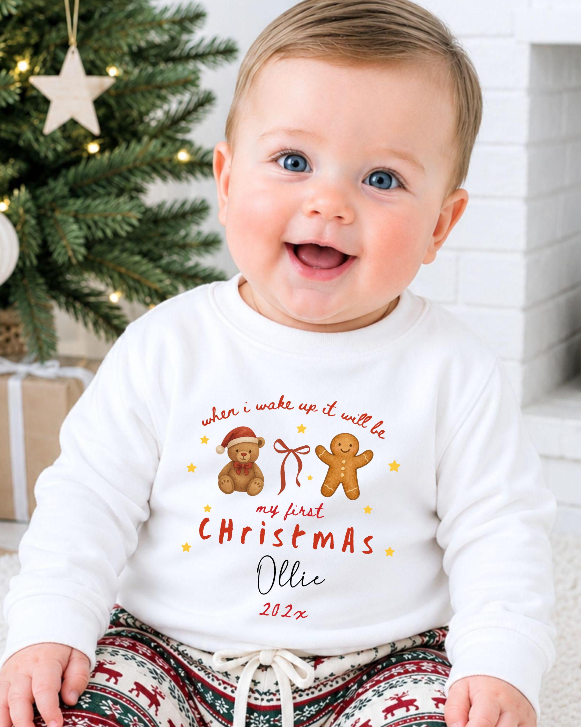 A smiling baby wearing a white long-sleeved shirt with a Christmas-themed design and text.
