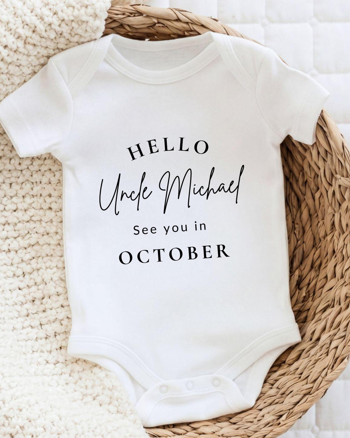 A white baby onesie with text printed on it, placed on a woven basket.