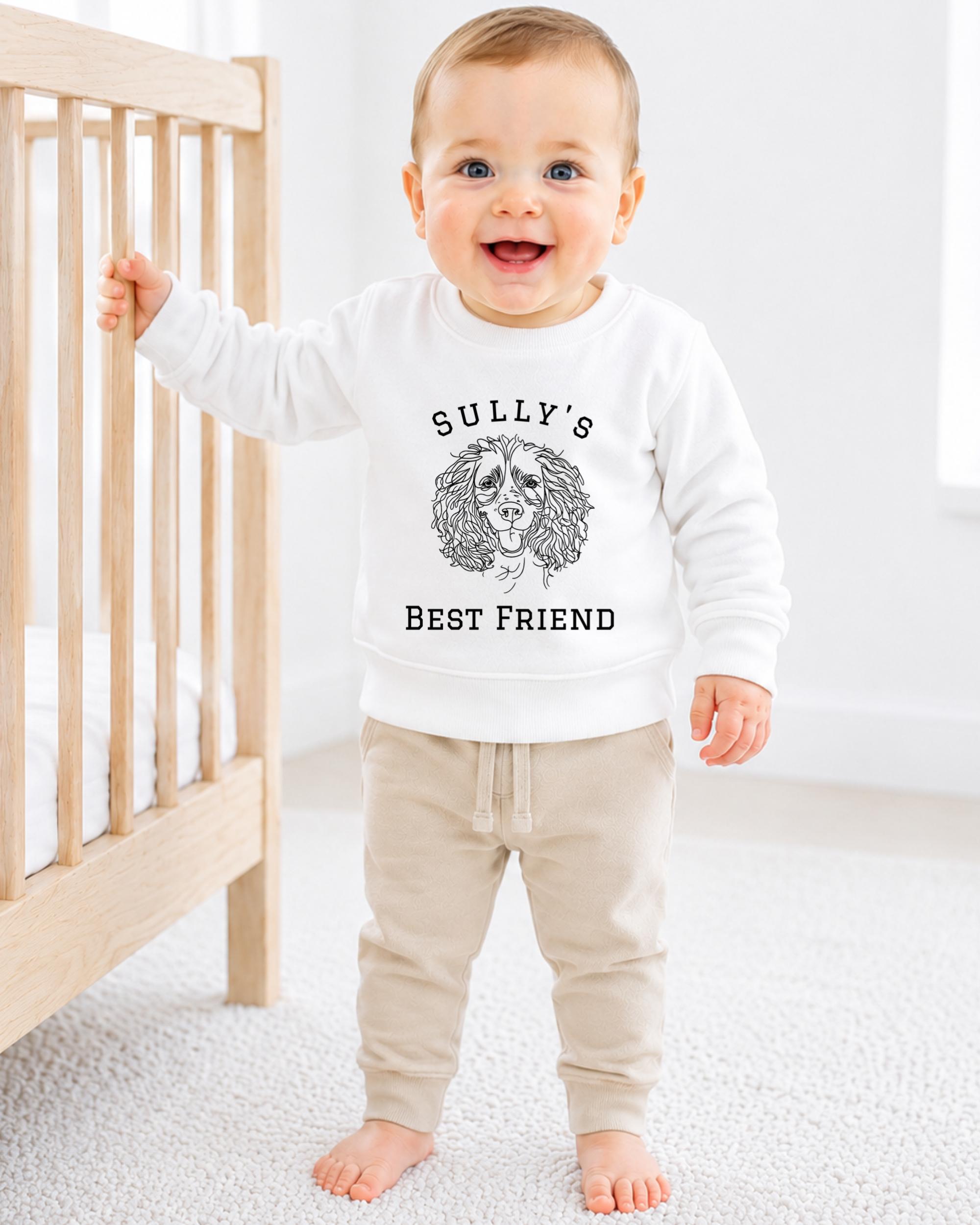 A smiling baby boy wearing a white sweatshirt with the text "SULLY'S BEST FRIEND" printed on it.