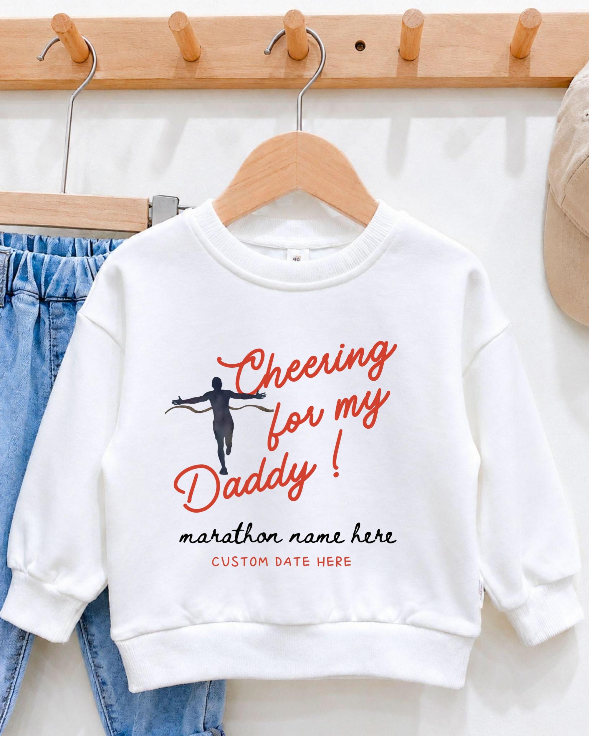 A white sweatshirt with a graphic design and text printed on it, hanging on a wooden hanger.