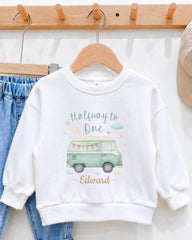A white sweatshirt with a graphic design of a van and the text "Halfway to One" printed on it, hanging on a wooden hanger.