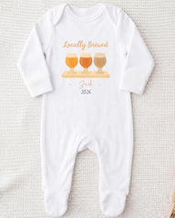 A white onesie with a graphic design of three beer glasses and the text "Locally Brewed Jack 2026" printed on it.