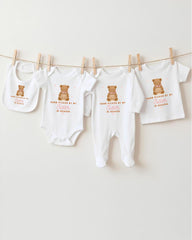 A collection of baby clothes, including onesies and bibs, hanging on a clothesline.