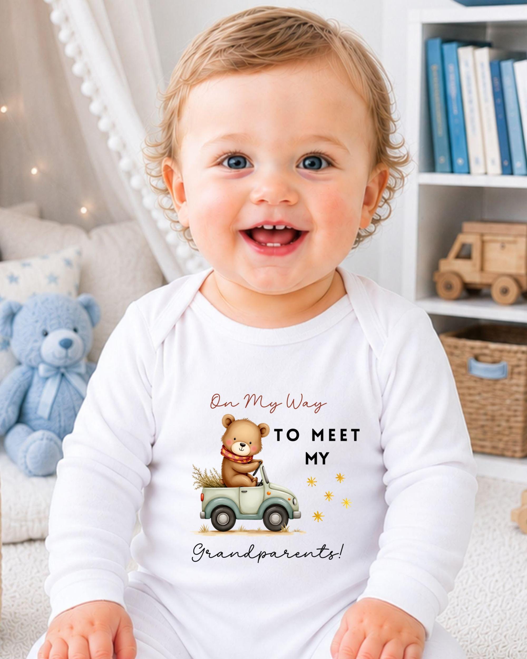 A smiling baby wearing a white onesie with a cartoon bear and the text "On My Way to Meet My Grandparents!"