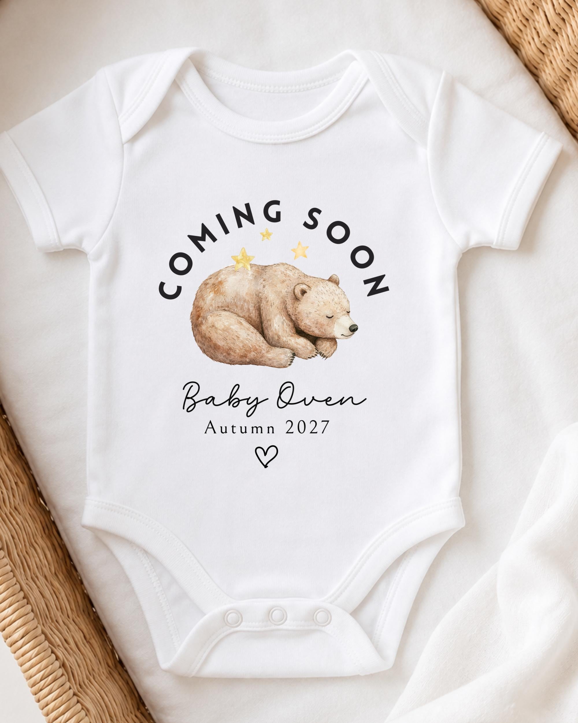 A white baby onesie with a graphic of a sleeping bear and text that says "Coming soon Baby Owen Autumn 2027".