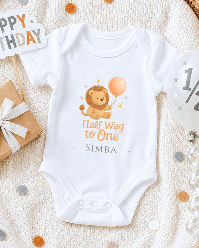 A white onesie with a cartoon lion and a balloon, along with a "Happy Birthday Simba" sign, is displayed on a white blanket.