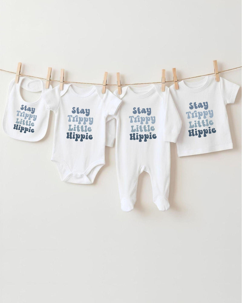 A row of four white baby clothes with the text "Stay Trippy Little Hippie" printed on them, hanging on a clothesline.