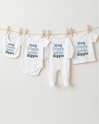 A row of four white baby clothes with the text "Stay Trippy Little Hippie" printed on them, hanging on a clothesline.