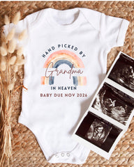 A white baby onesie with a rainbow graphic and text that says "HAND PICKED BY Grandma in Heaven BABY DUE NOV 2026" is displayed alongside a set of three black and white baby ultrasound images.