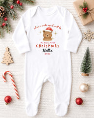 A white onesie with a bear and Christmas text, surrounded by Christmas decorations and ornaments.