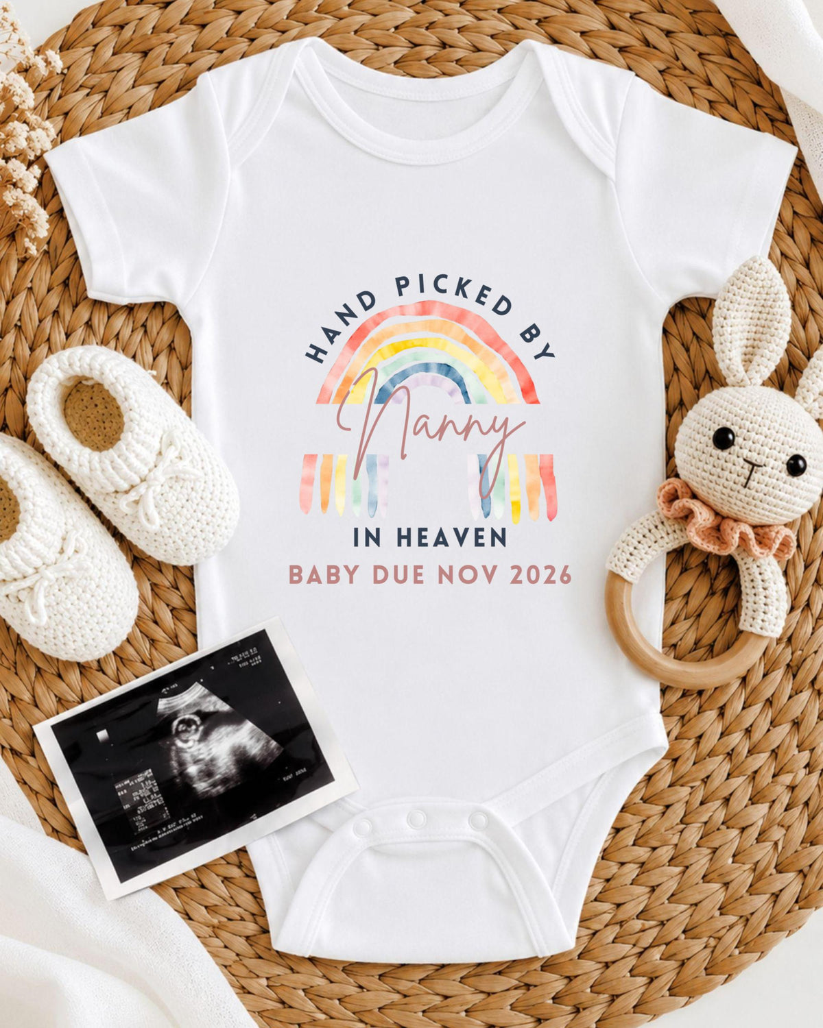 A baby onesie with a rainbow design and text, a pair of white crocheted bunny slippers, and an Ultrasound image of a baby.