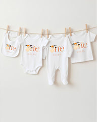 A collection of four white baby clothes, including bibs and onesies, hanging on a clothesline.