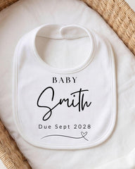 A white baby bib with personalized text and a date printed on it.