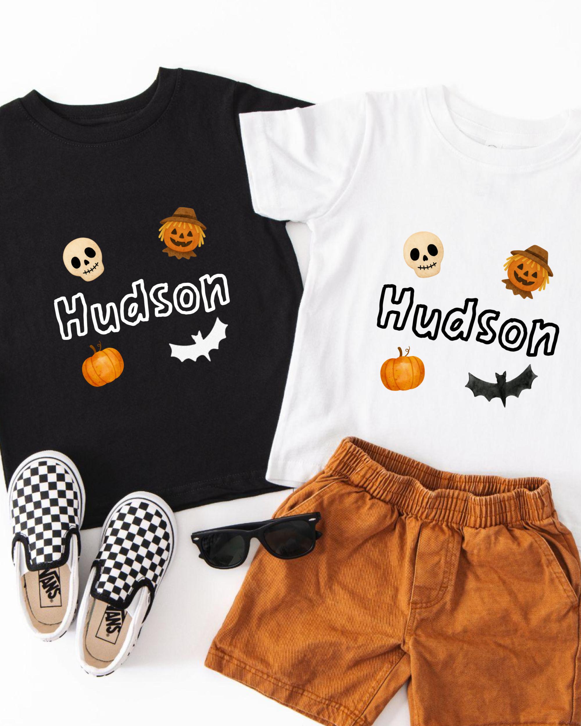 A black t-shirt with the name "Hudson" printed on it, a white t-shirt with the same name, a pair of brown shorts, a pair of black and white checkered shoes, and a pair of sunglasses.