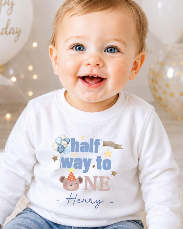 A smiling baby boy wearing a white shirt with a birthday message and a cartoon character.