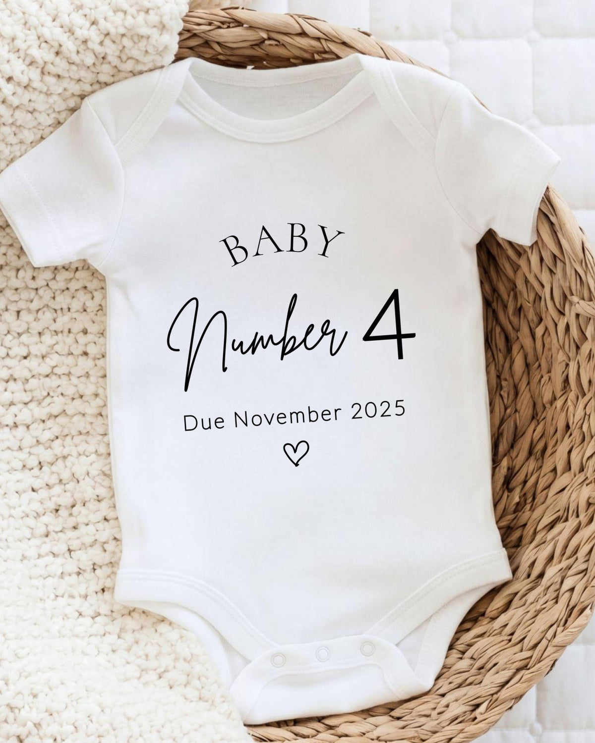 A white baby onesie with the text "BABY Number 4 Due November 2025" printed on it.