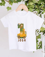 A white t-shirt with a cartoon image of a giraffe and a monkey on a yellow truck, along with the text "JOSH" printed on it.
