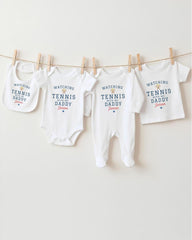 A row of four white baby clothes with the text "WATCHING TENNIS DADDY Jackson" printed on them, hanging on a clothesline.