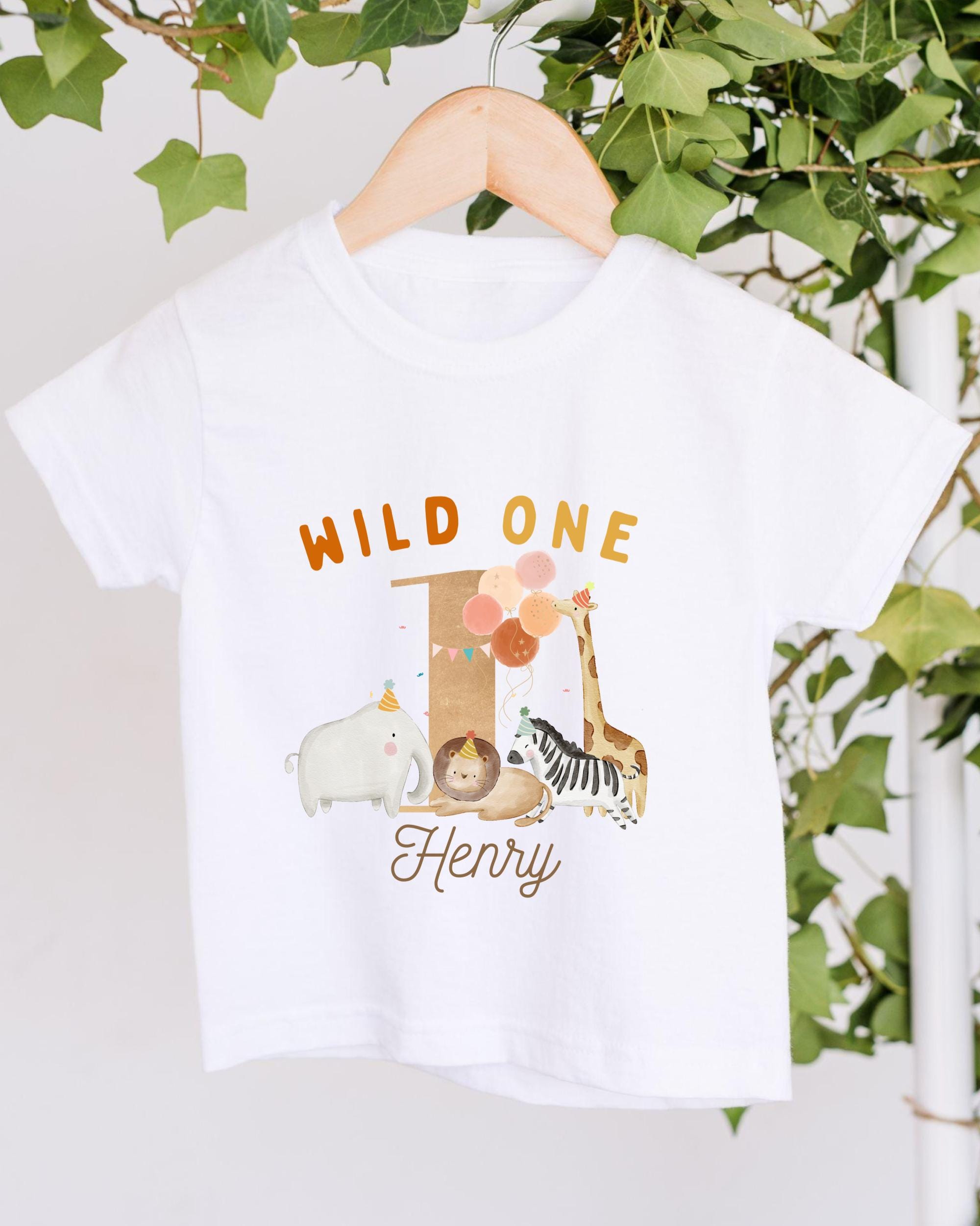 A white t-shirt with a graphic design featuring a giraffe, elephant, and other animals, along with the text "Wild One Henry".
