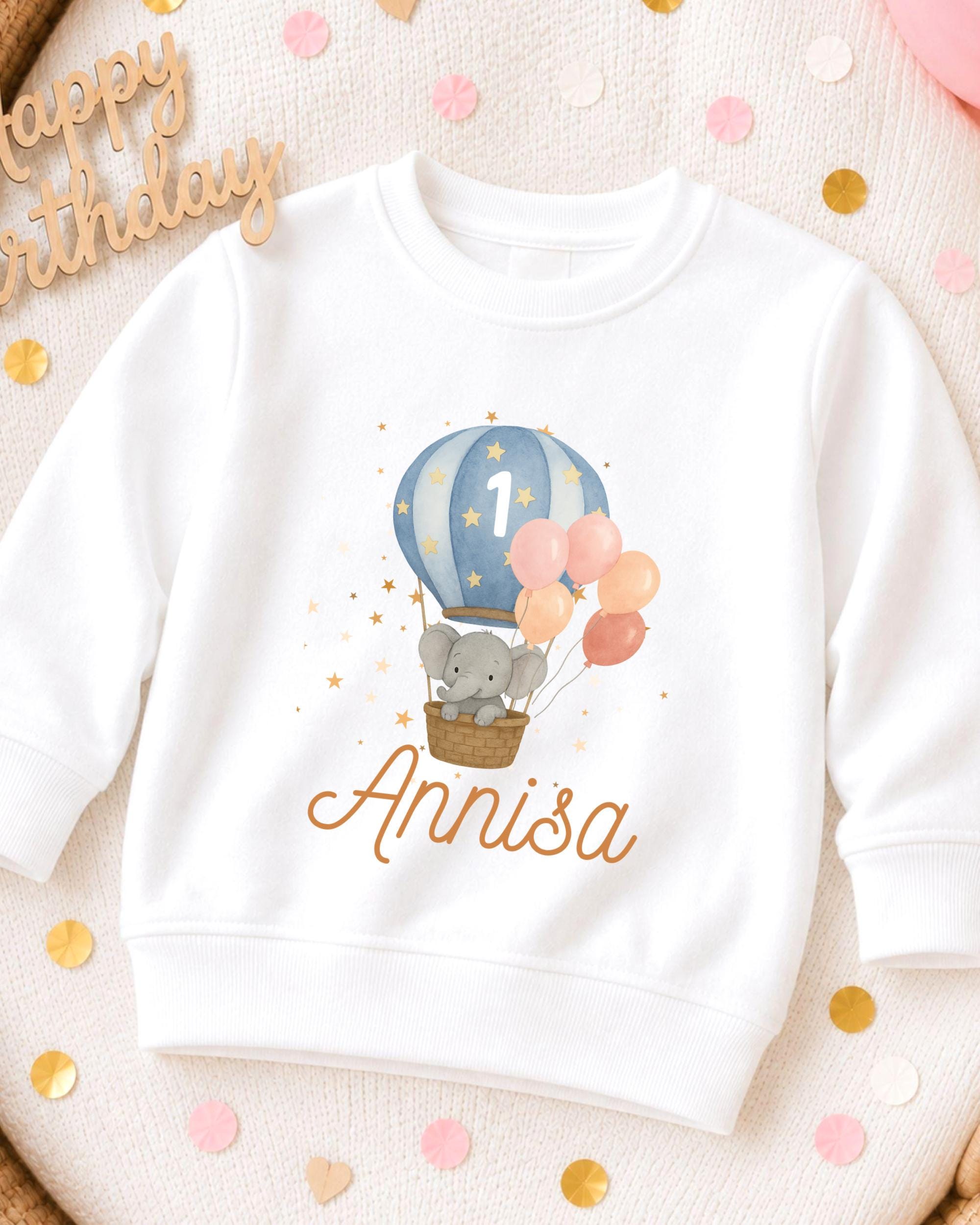 A white sweatshirt with a cartoon elephant and a hot air balloon design, along with the name 'Annisa' printed on it.