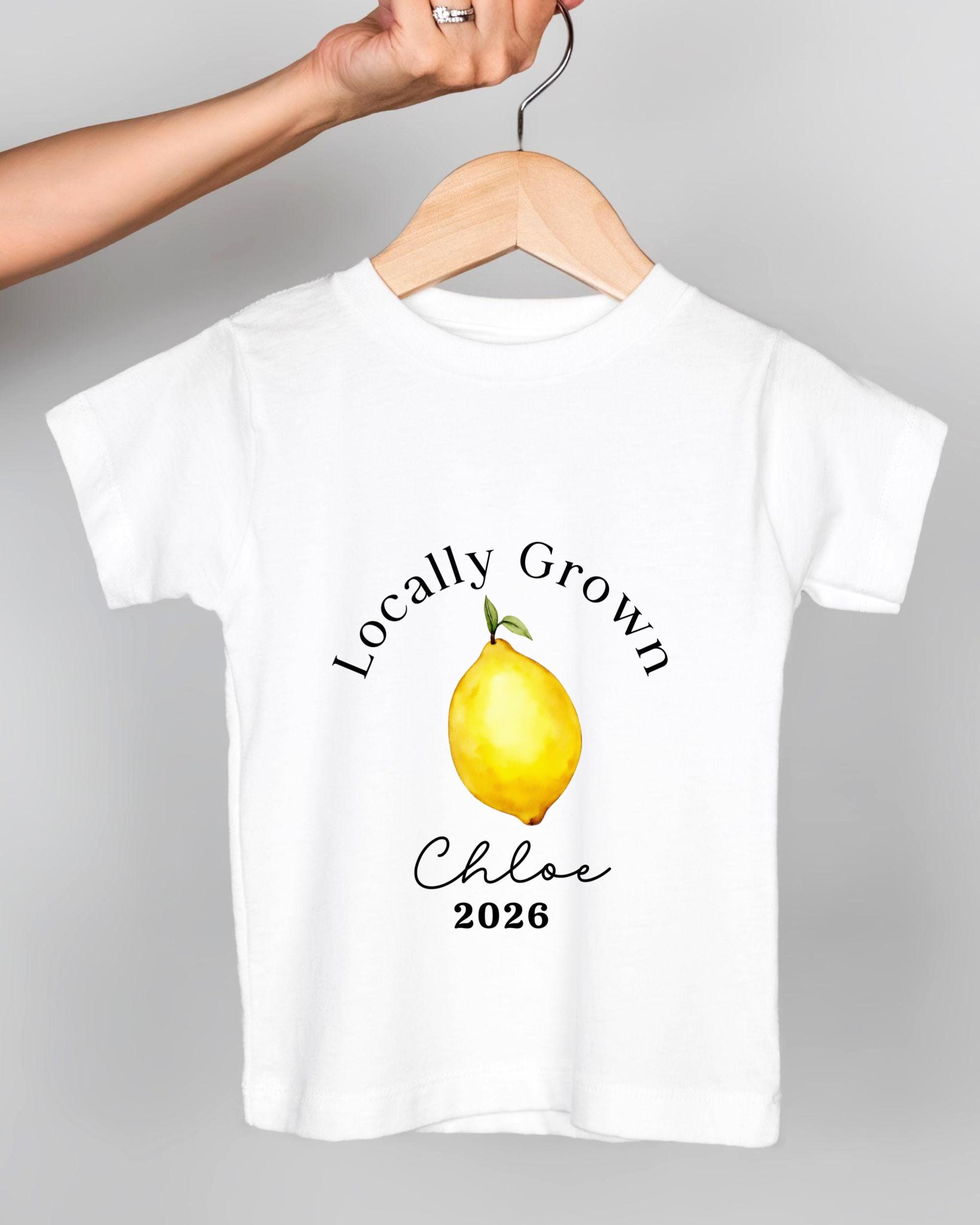 A white t-shirt with a printed design of a lemon and the text "Locally Grown Chloe 2026" printed on it.
