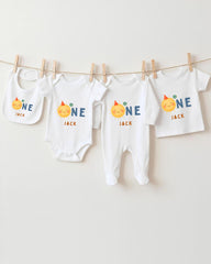 A collection of four white baby clothes, including onesies and pajamas, with the name "Jack" printed on them. The clothes are hanging on a clothesline, with the clothespins holding them in place.