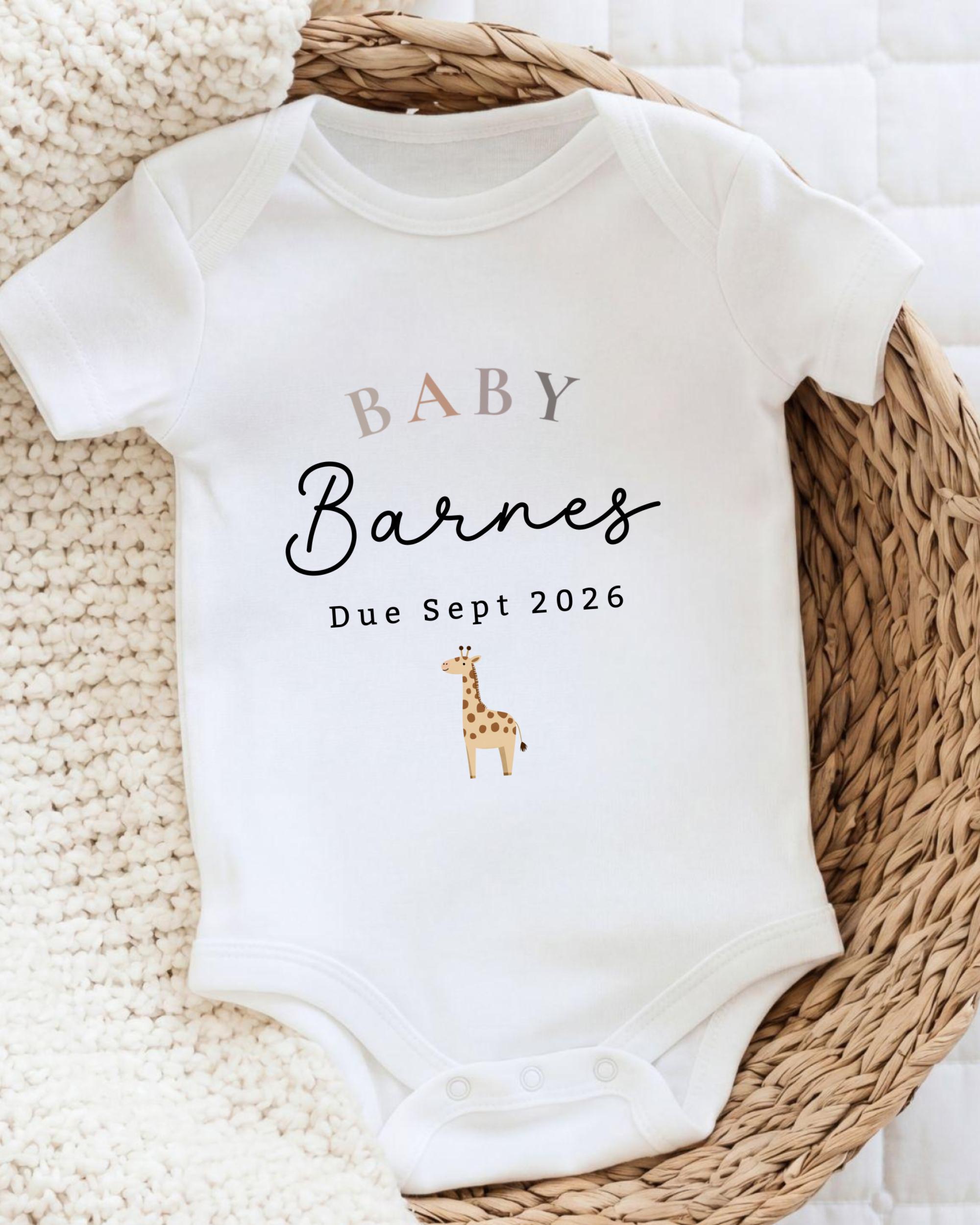 A white baby onesie with the text "BABY Barnes Due Sept 2026" printed on it, along with a small illustration of a giraffe.