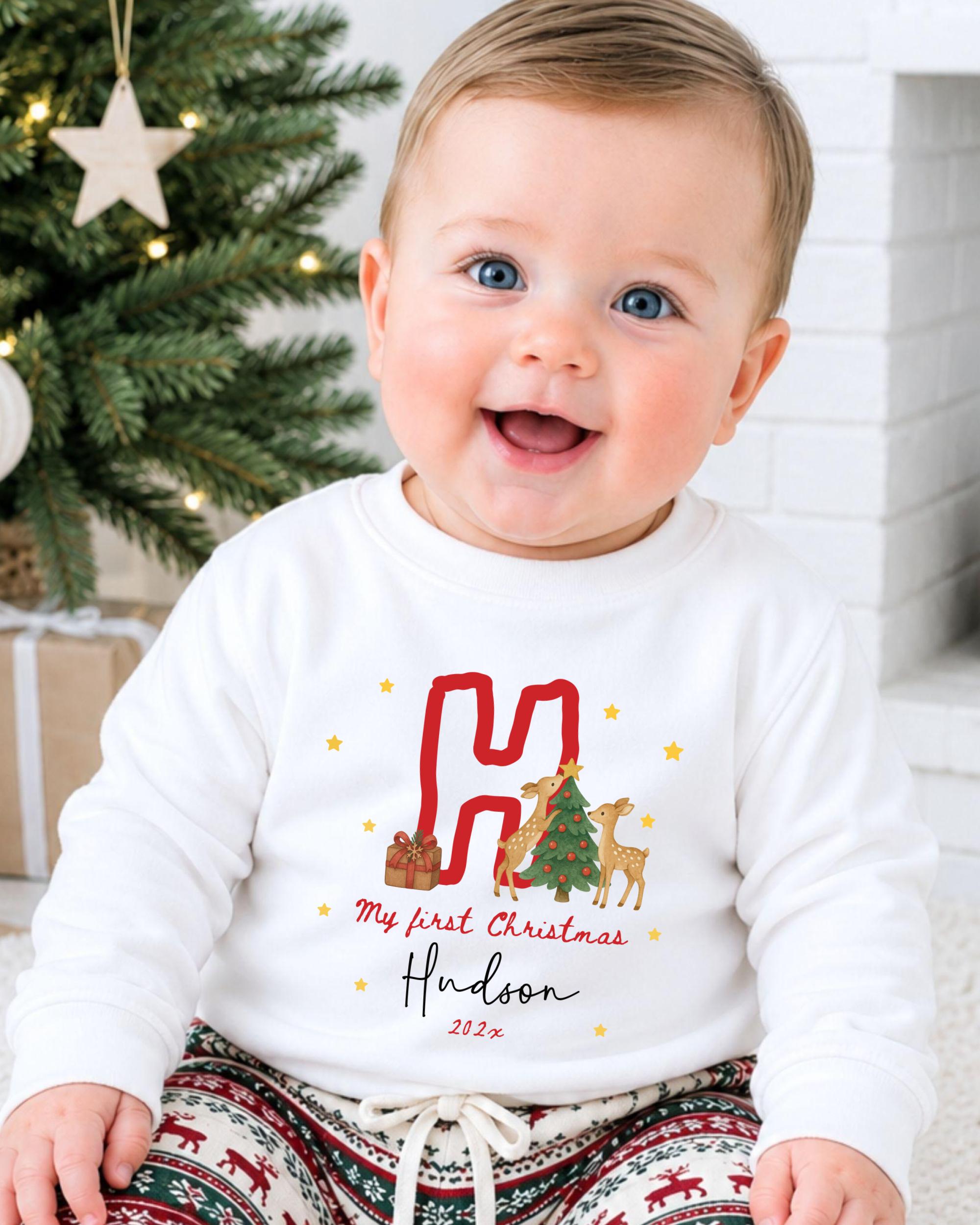 A smiling baby boy wearing a white sweatshirt with a personalized Christmas-themed design.